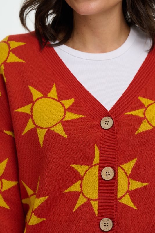 Close up of Red cardigan with yellow sun patterns and button details worn by a person.