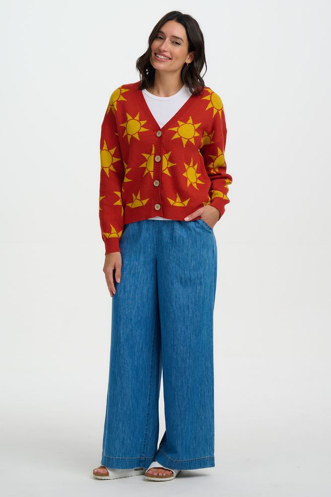 Woman wearing a red cardigan with yellow sun patterns and blue jeans on a white background