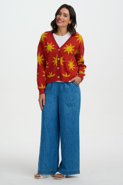 Woman wearing a red cardigan with yellow sun patterns and blue jeans on a white background