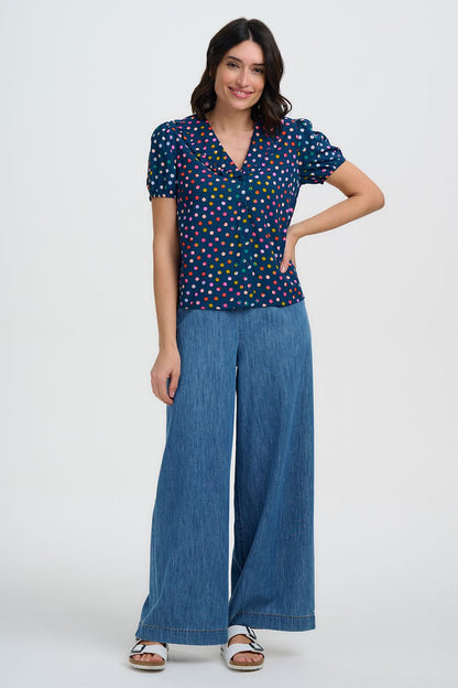 Woman wearing a navy polka dot top and wide-leg blue pants with one arm on hip on a white background