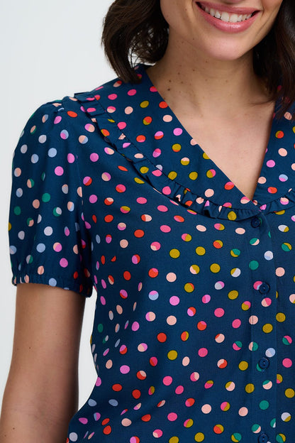 Woman wearing a navy dress with colorful polka dots on a plain background