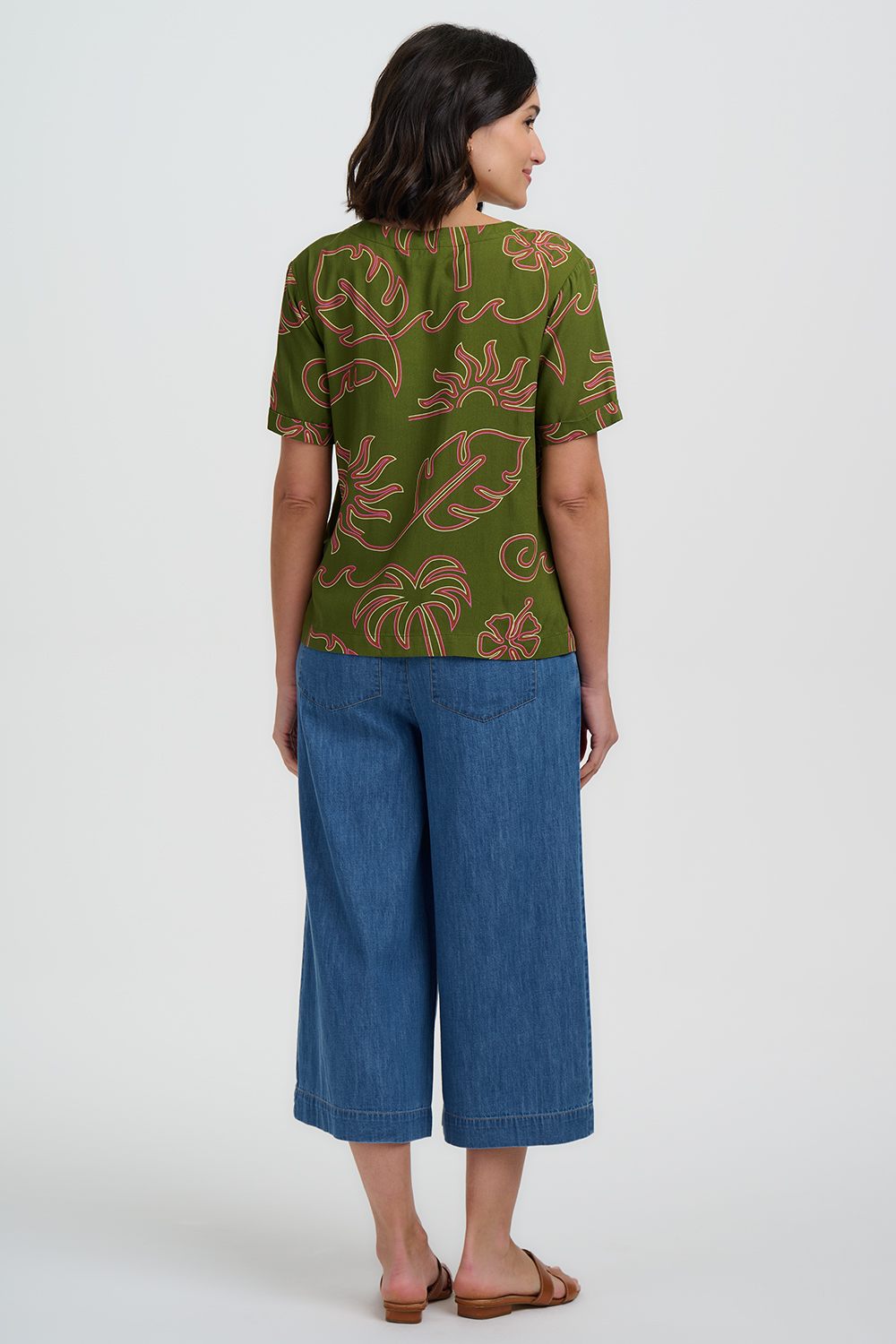Woman wearing a green patterned top and blue jeans on a white background