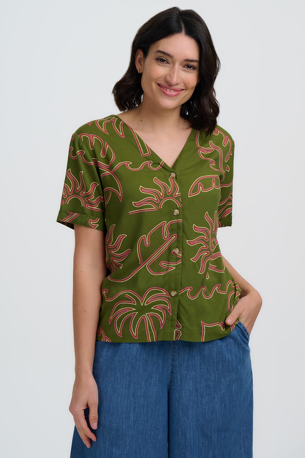 Woman wearing a green patterned blouse with blue pants on a white background