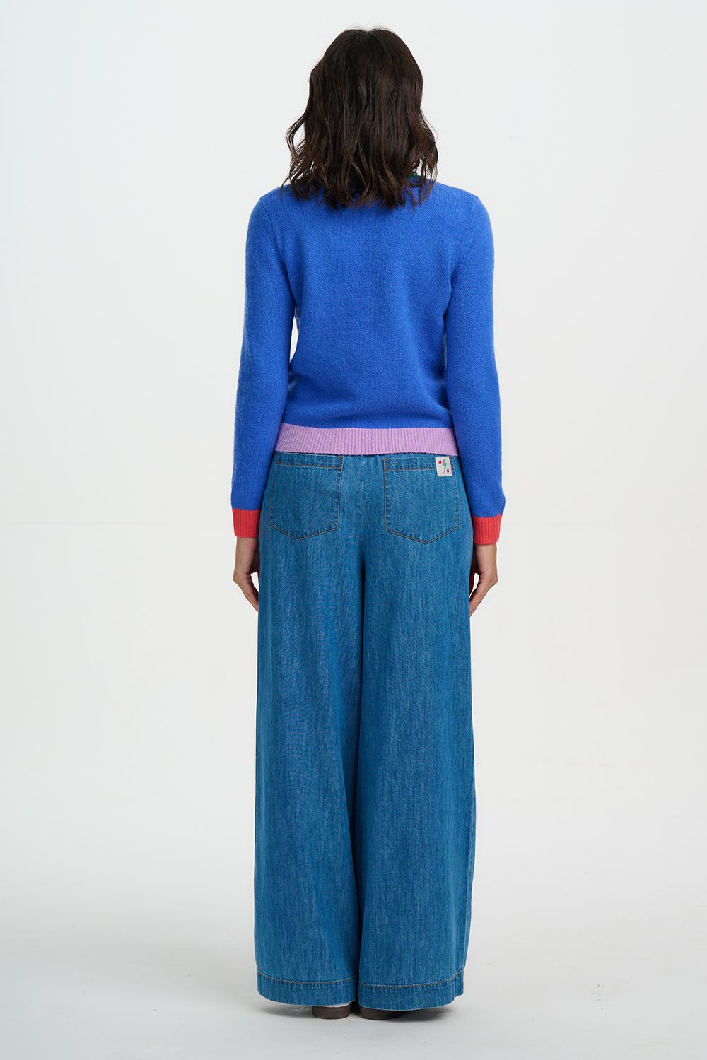 Person wearing a blue sweater and wide-leg jeans on a white background