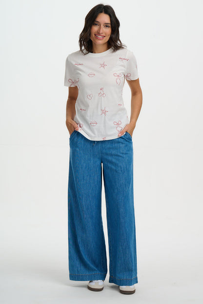 Woman wearing a white t-shirt with red patterns and blue pants on a white background