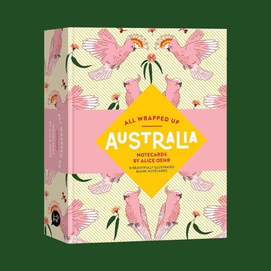 All Wrapped Up: Australia notecards box by Alice Oehr, featuring a pink and yellow cockatoo pattern with a central yellow diamond label, shown on a dark green background.