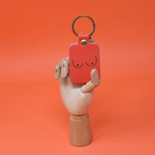 Styled image of a coral-Red keychain with a smiley face held by a wooden hand against an orange background