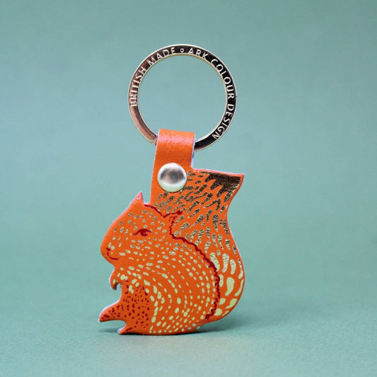Orange squirrel-shaped keychain with a gold ring on a teal background