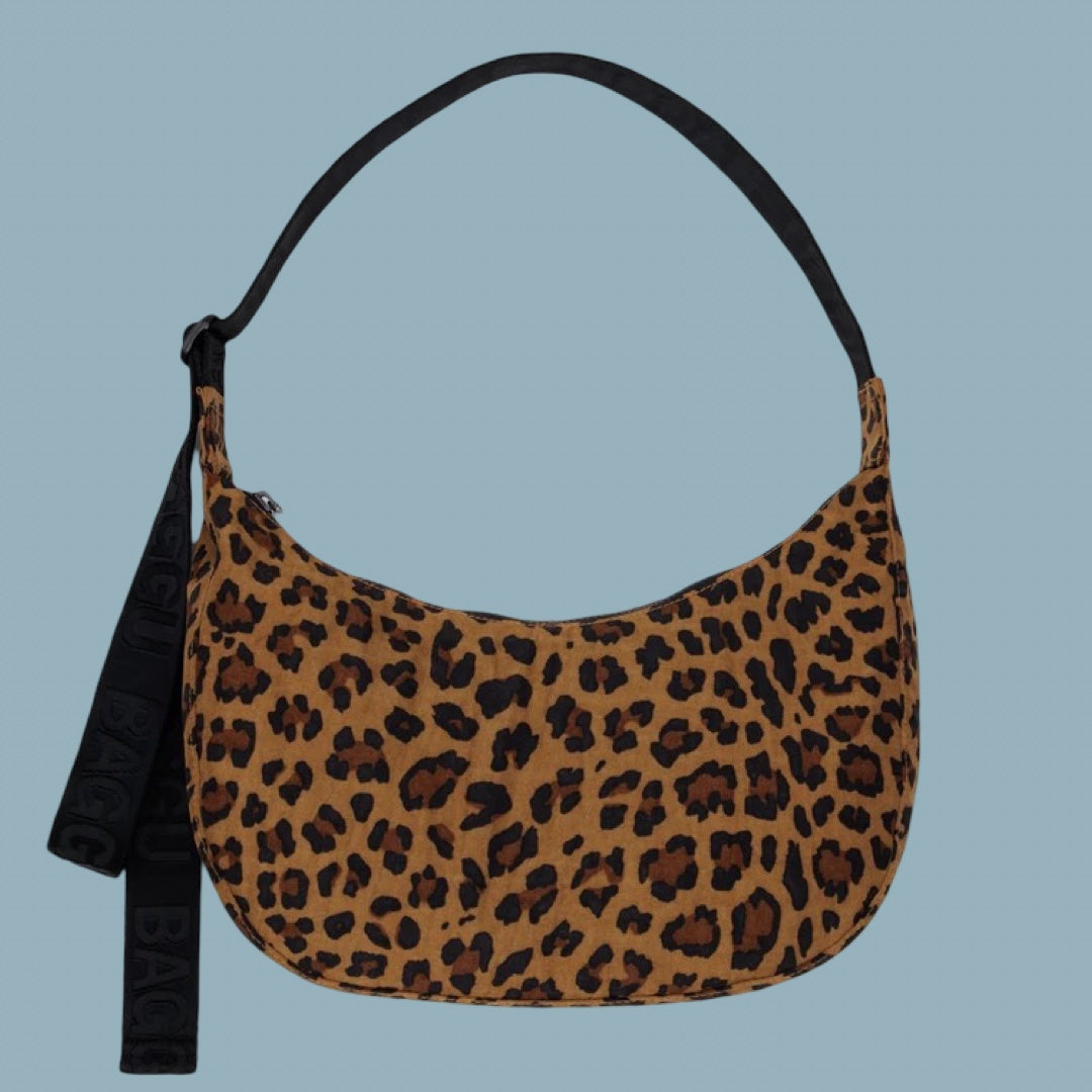 A Baggu Medium Nylon Crescent Bag in Leopard, a leopard print crescent shoulder bag with a black strap, shown against a solid light blue background.
