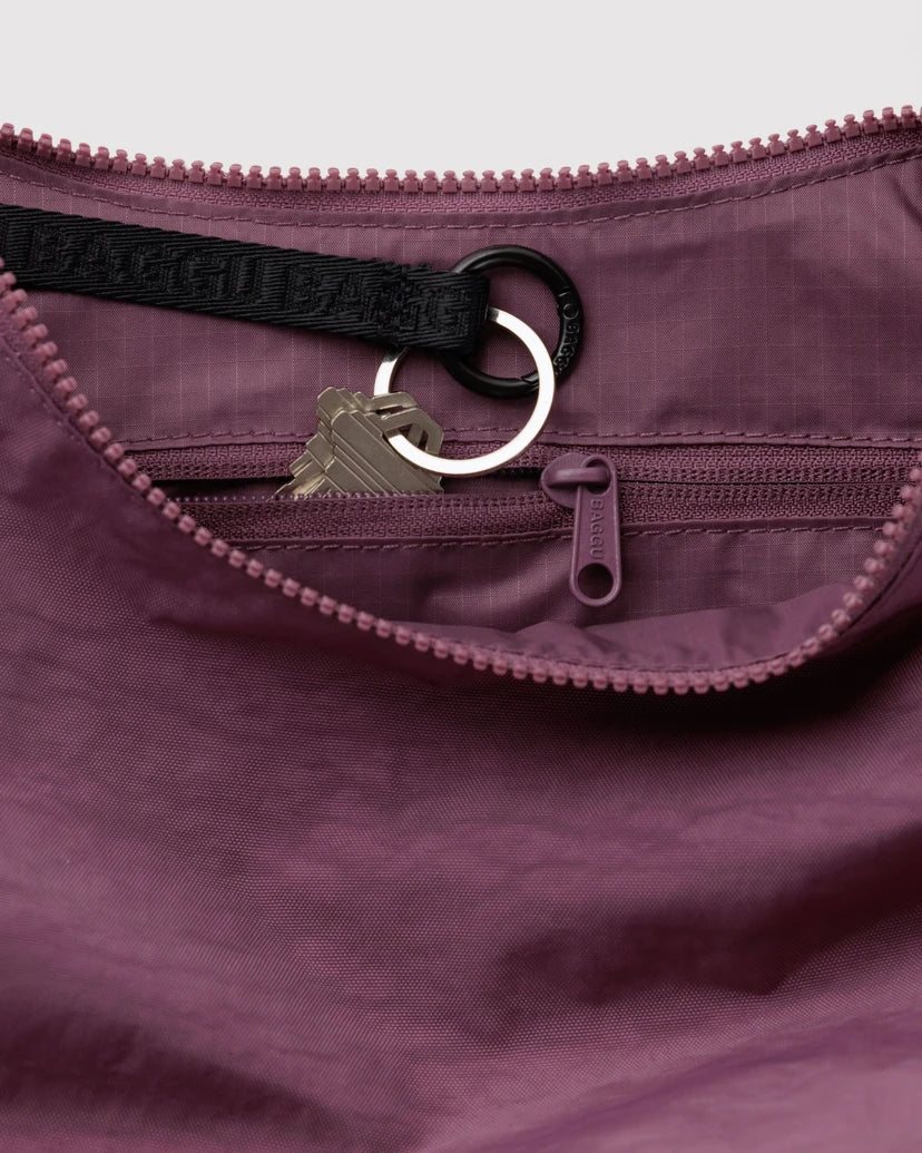 Close-up of a dusty purple nylon bag showing the interior zippered pocket with a black branded web strap, metal keyring, and zipper pull.