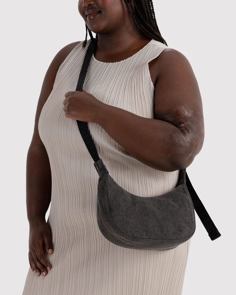 A woman wearing a ribbed cream dress carries a dark gray crescent-shaped shoulder bag with a black strap against a light gray studio background.