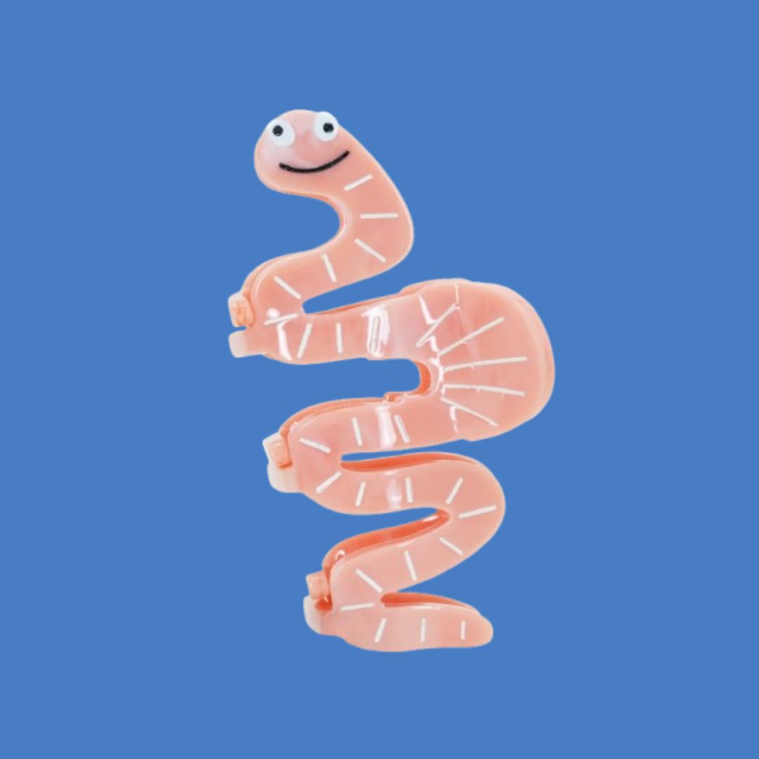 A novelty pink hair claw clip shaped like a smiling worm, shown on a solid blue background.
