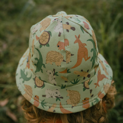 Back view of a Toddler wearing an Australian animal patterned bucket hat in a grassy setting
