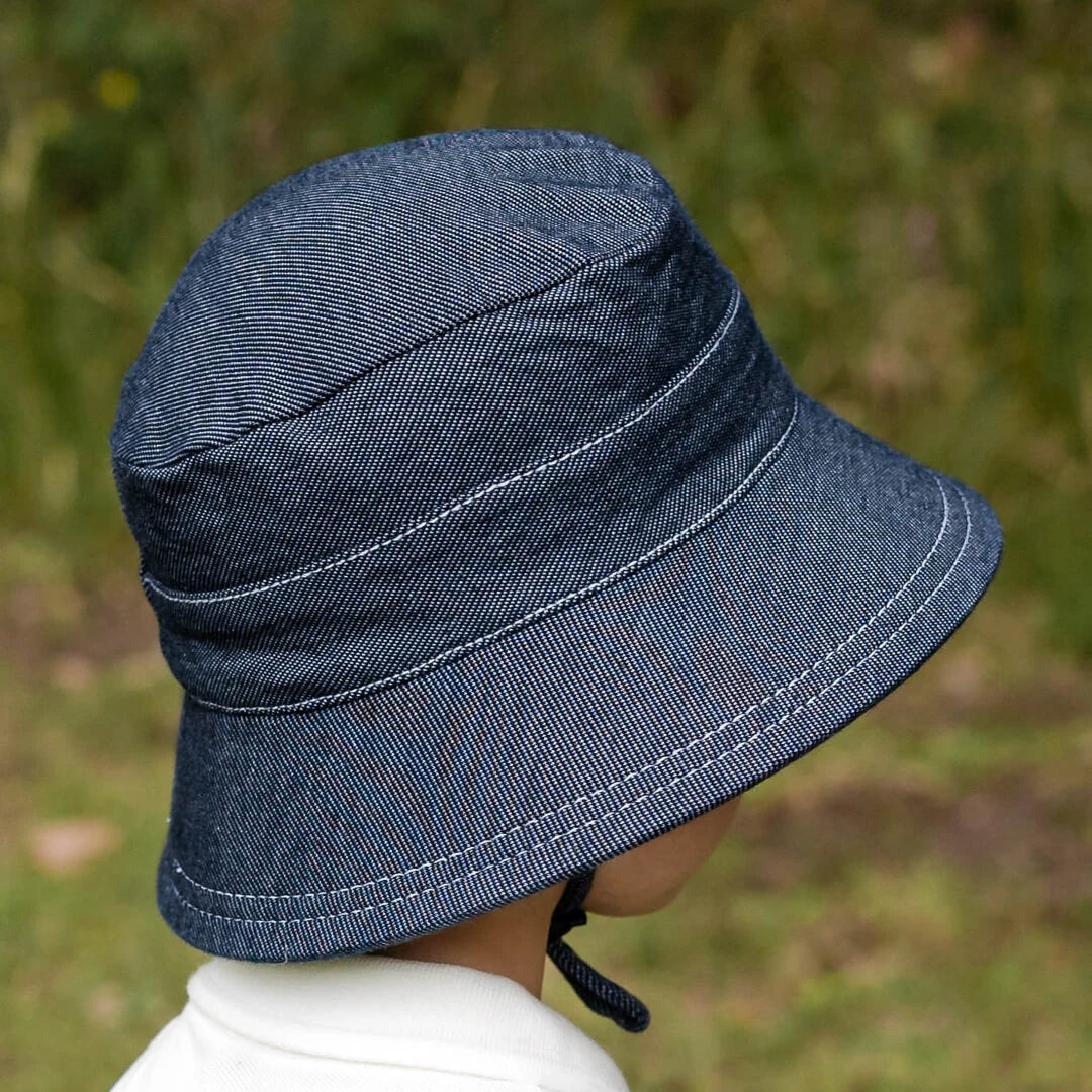 Side view of Blue-black denim bucket hat worn by a child against a blurred natural background
