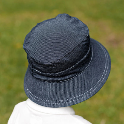 Back view of Blue-black denim bucket hat worn by child on a blurred green background