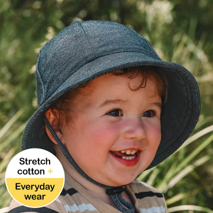 Toddler wearing a denim hat with a green blurred background
