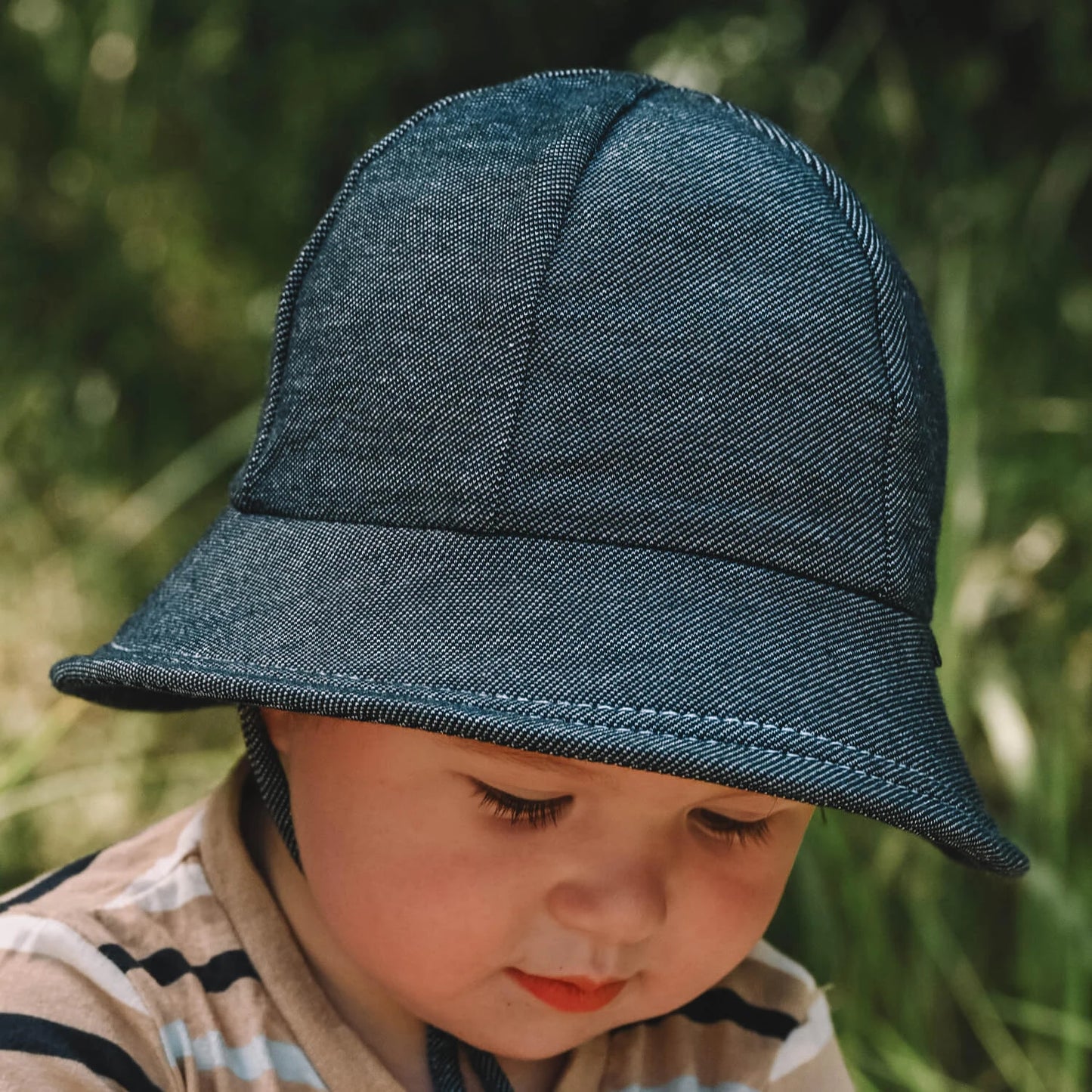 Toddler wearing a blue-black denim hat with a blurred green background