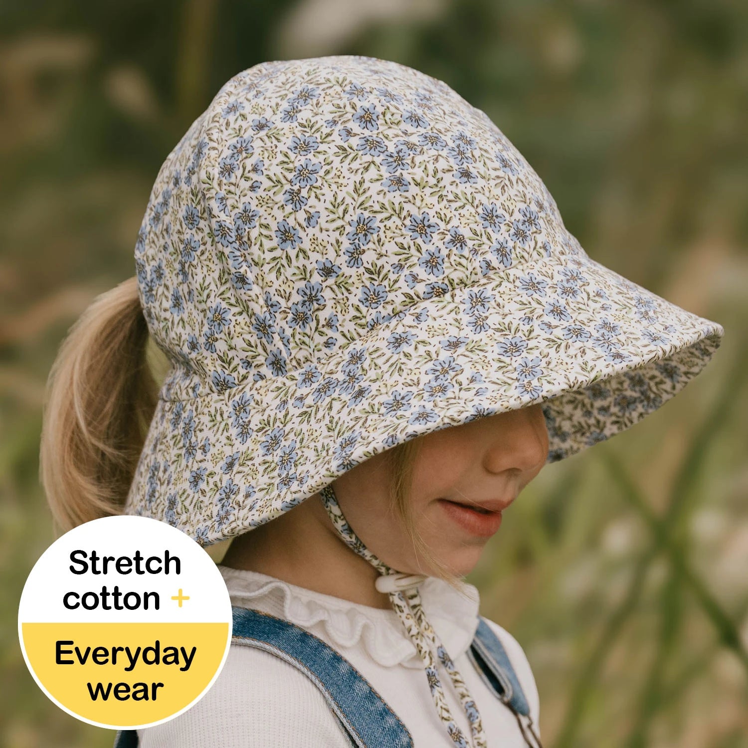 Side view of Child wearing a floral sun hat with a ponytail slit in the back with text 'Stretch cotton + Everyday wear' in the corner.
