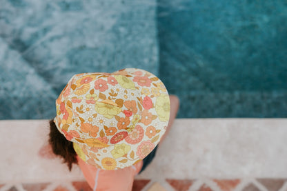 top view of Bedhead Tallulah Swim Bucket Hat worn by a young model sitting on the edge of a swimming pool