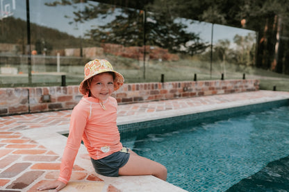 front view of Bedhead Tallulah Swim Bucket Hat worn by a young model sitting on the edge of a swimming pool
