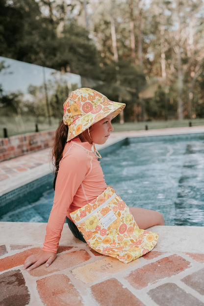 Side view of Bedhead Tallulah Swim Bucket Hat worn by a young model sitting on the edge of a swimming pool