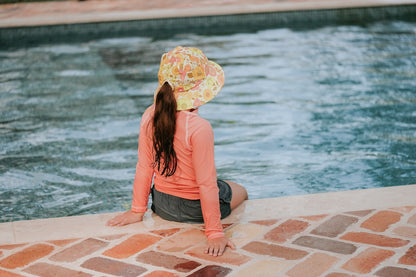 Back view of Bedhead Tallulah Swim Bucket Hat worn by a young model with ponytail through the back of the hat, and sitting on the edge of a swimming pool