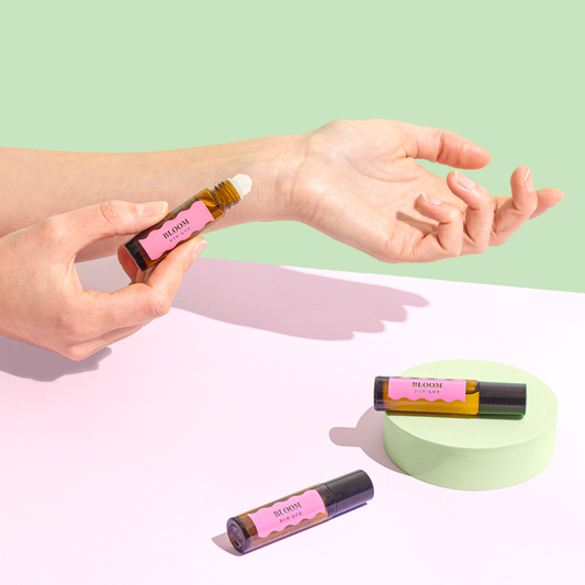 A pair of hands showing off a bottle of Bon Lux Bloom Natural Perfume, and two other bottles of the perfume are lying on a table. 