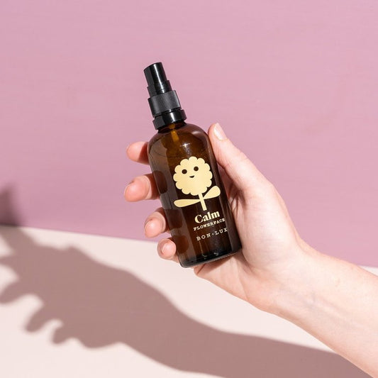 Hand holding a bottle of Bon Lux Flowerface Face Mist in Calm against a pink background.