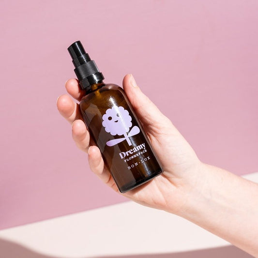 Hand holding a bottle of Bon Lux Flowerface Face Mist in Dreamy against a pink background.