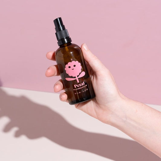 Hand holding a bottle of Bon Lux Flowerface Face Mist in Petal against a pink background.