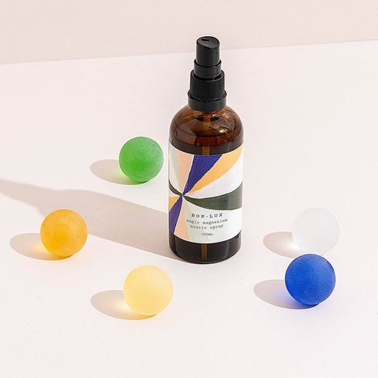 A bottle of Bon Lux Muscle Magic Magnesium Spray with colourfully balls around it on a light surface
