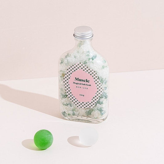 A bottle of Bon Lux Muscle Magical Salt Soak with a green ball and a white ball on a light background.