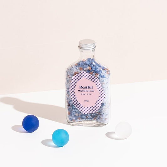 A bottle of Bon Lux Restful Magical Salt Soak with two blue balls and a white ball on a light background.