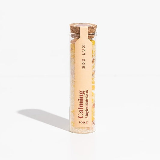 A glass tube of Bon Lux Calming Magical Salt Soak containing yellow bath salts on a white background