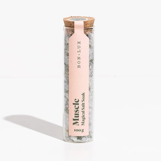A glass tube of Bon Lux Muscle Magical Salt Soak containing green bath salts on a white background