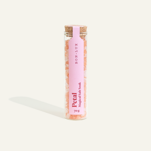 A glass tube of Bon Lux Petal Magical Salt Soak containing pink bath salts on a white background