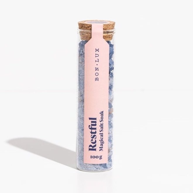 A glass tube Bon Lux Restful Magical Salt Soak containing blue bath salts on a white background