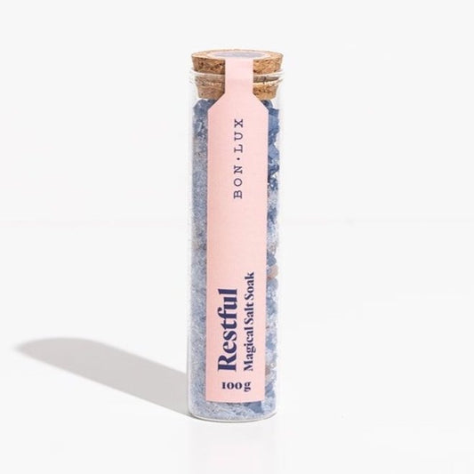 A glass tube Bon Lux Restful Magical Salt Soak containing blue bath salts on a white background