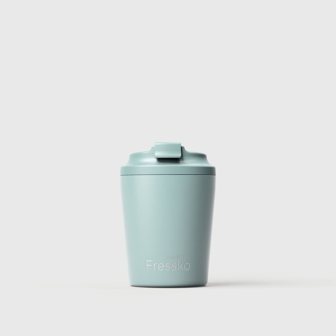 A light sea foam blue-green insulated travel tumbler with a matching flip-top lid, featuring the 'Fressko' brand name printed in white near the bottom, set against a clean, light gray studio background.