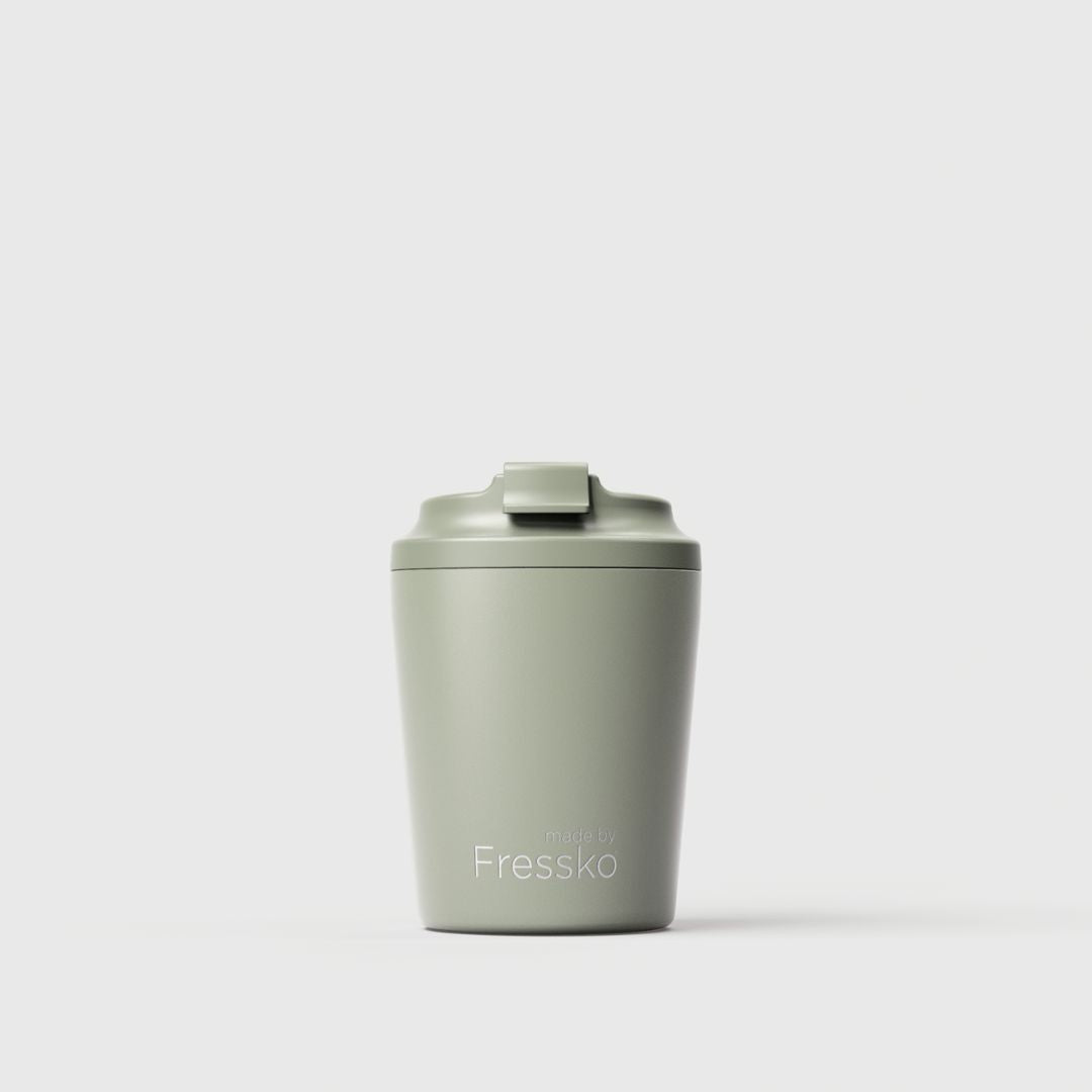 A matte light sage green insulated travel tumbler with a matching flip-top lid, featuring the Fressko brand name printed in white near the bottom, set against a clean light gray background.