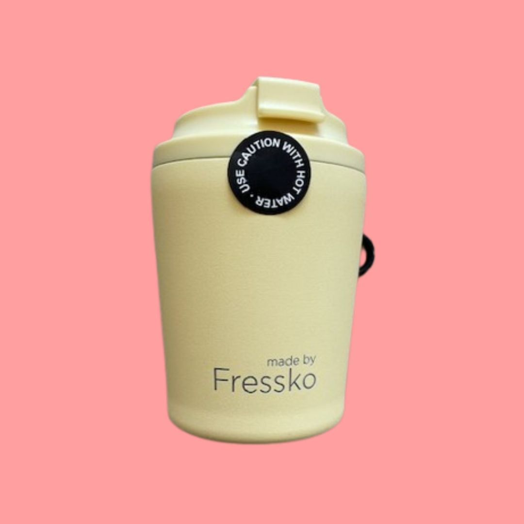 Light yellow reusable cup with black caution label on a pink background, featuring 'made by Fressko' branding.