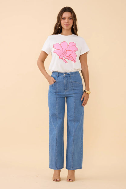Woman wearing a white t-shirt with a pink floral design and blue jeans on a beige background