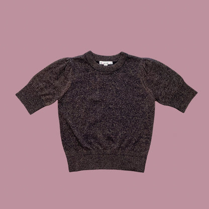 Frock Me Out Lurex Knit, a short-sleeved knit with puff sleeves in Black with bronze lurex thread throughout, on a powder pink background.