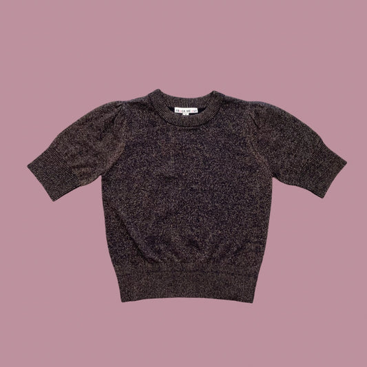 Frock Me Out Lurex Knit, a short-sleeved knit with puff sleeves in Black with bronze lurex thread throughout, on a powder pink background.