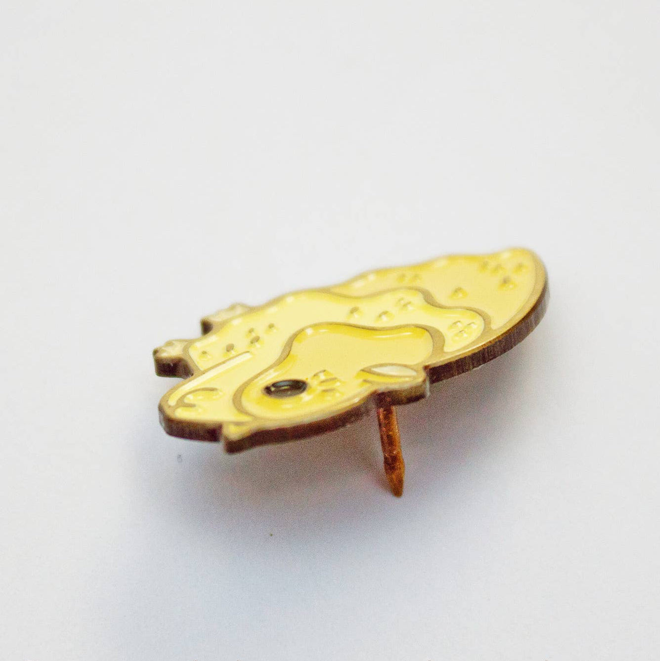 A small enamel pin shaped like a stylized cat head, featuring a gold-toned metal outline and a pale yellow enamel fill, photographed on a plain white background.