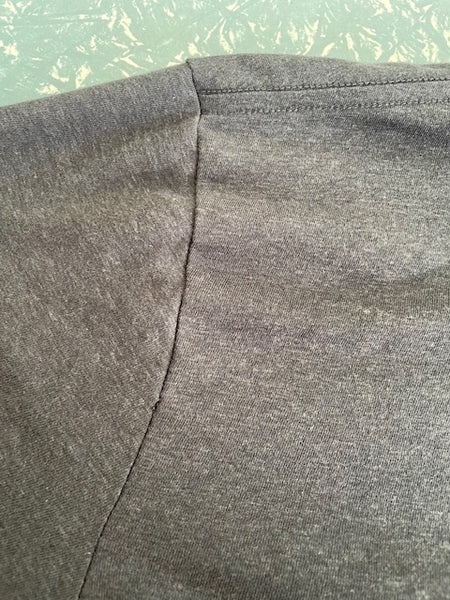 Close up of the back of the tee's left arm seam with the small hole.