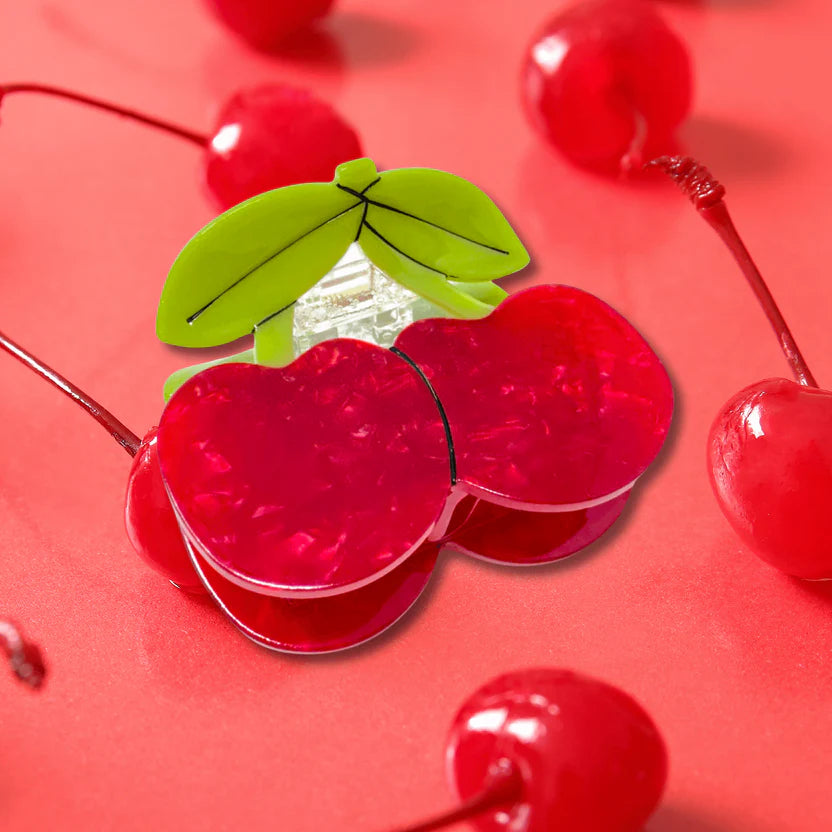Red cherry-shaped hair clip with green leaves on a red background