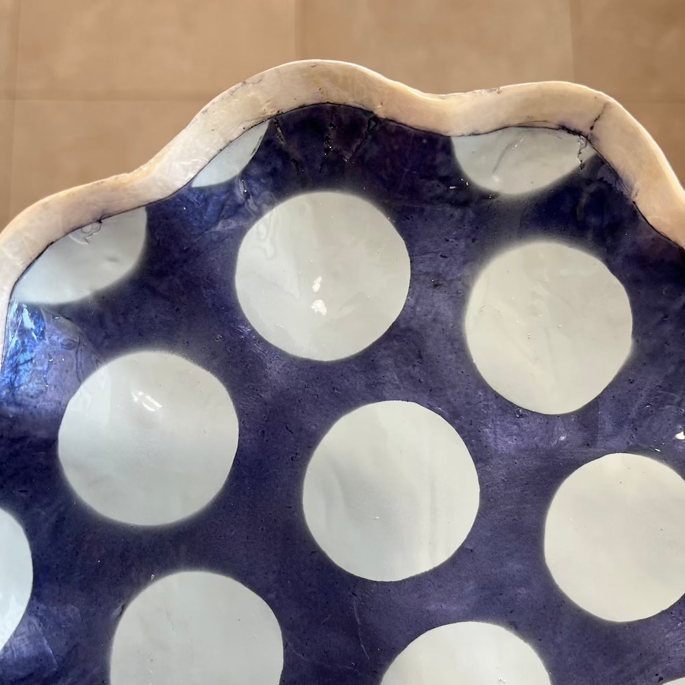 Shell dish with scalloped edge and white polka dots on a blue background