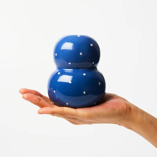 Blue ceramic object with white dots held in a hand against a white background