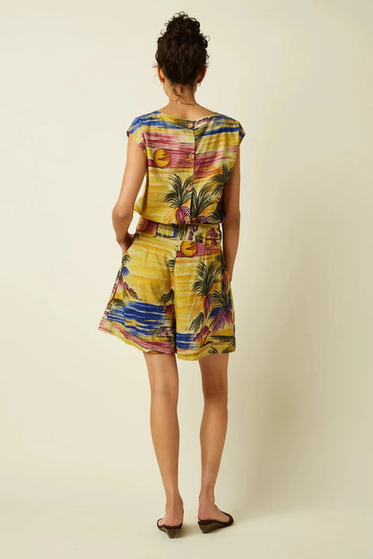 Woman shown from behind wearing a colourful, vintage-inspired tropical print top and shorts on a plain beige background